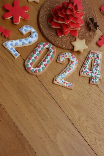 Christmas tree made of star shaped shortcrust cookies with red sugar glaze and cookies in form of numbers 2024 on wooden table