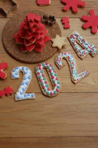 Christmas tree made of star shaped shortcrust cookies with red sugar glaze and cookies in form of numbers 2024 on wooden table