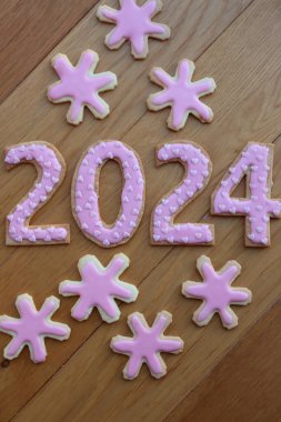 Kısa hamurlu kurabiyeler ve 2024 numaralı pembe kalp parçacıkları ve ahşap masada kar tanesi kurabiyeleri.
