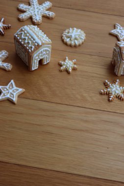 Beyaz kremalı küçük zencefilli evler yıldız şeklinde zencefilli kurabiyeler ve ahşap masada kar taneleri. 