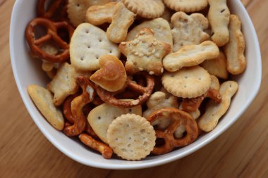 Beyaz bir kasede çeşitli atıştırmalıklar: tuzlu kraker, tohumlu kraker ve ahşap masa üzerinde bitki. Çeşitli parti yemekleri.