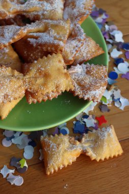 Masada yeşil bir tabakta fiyonk şeklinde kızartılmış İtalyan tatlısı. Chiacchere veya crostoli, bugie, renkli kağıt konfetiyle cenci 