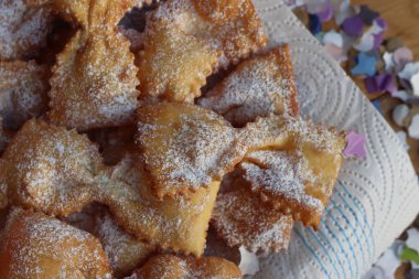 Masadaki tabakta fiyonk şeklinde kızartılmış İtalyan tatlısı. Chiacchere veya crostoli, bugie, cenci konfeti ve kağıt serpentine