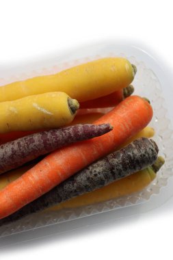 Beyaz arka planda plastik kutuda farklı renkte havuçlar var. Organik sağlıklı gökkuşağı havuçları 