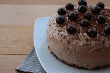 Çikolatalı keki, kakao kremalı ve ekşi kirazlı yakın plan beyaz bir tabakta, ahşap bir masada.