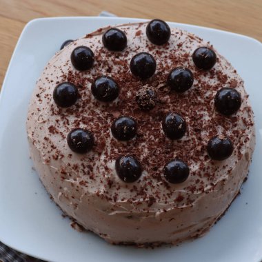 Çikolatalı pastanın üst görüntüsü kakao kremalı ve şerbetli kirazlar ahşap bir tabakta beyaz bir tabakta.