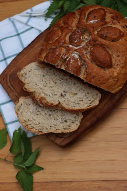 Pişmiş ev yapımı ekmeğin üst görüntüsü. Tahta masada ısırgan otları ve taze bitkilerle dilimlenmiş.