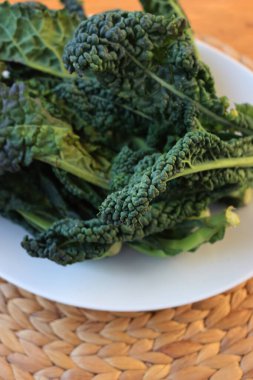 Fresh tuscan kale leaves on a white plate on wooden table. Cavolo nero lacinato or Brassica oleracea var. palmifolia  clipart