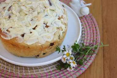 Paskalya için badem ve beyaz çikolata jöleli yuvarlak tatlı ekmek. Tahta masadaki beyaz tepside kır çiçekleriyle birlikte.