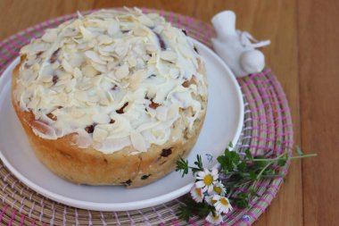 Paskalya için badem ve beyaz çikolata jöleli yuvarlak tatlı ekmek. Tahta masadaki beyaz tepside kır çiçekleriyle birlikte.