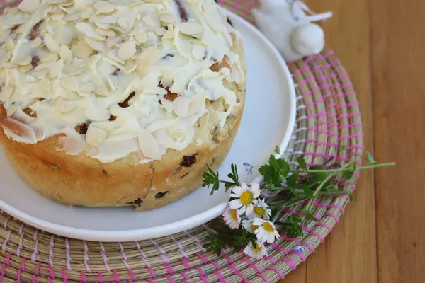 Paskalya için badem ve beyaz çikolata jöleli yuvarlak tatlı ekmek. Tahta masadaki beyaz tepside kır çiçekleriyle birlikte.