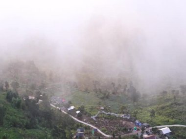Bereketli yeşilliklere yuva yapmış, dolambaçlı yolları ve dağınık evleri olan sisli bir kırsal köy.