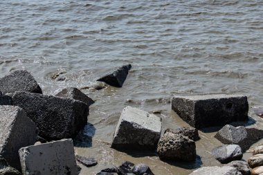 Patenga Deniz Sahili kıyılarına dağılmış beton bloklar doğal kıyı manzarasına endüstriyel bir kontrast oluşturur. Bu resim sert dokuları ve insan yapımı ile doğanın dinamik buluşmasını vurgular..