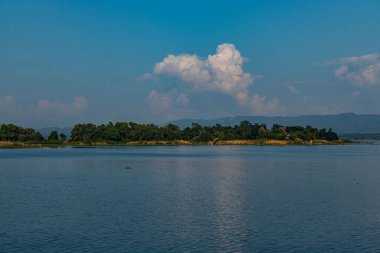 Kaptai Gölü 'nün kristal berrak suları çevresindeki yeşil tepeleri güzel bir şekilde yansıtarak huzurlu ve resimsel bir manzara yaratır. Bu sakin sahne doğanın, suyun ve yemyeşil çimlerin uyumunu yakalar..