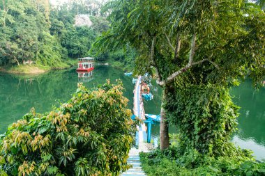 Kaptai Gölü 'nün sakin sularına yavaşça inen yeşil tepe yamaçlarının büyüleyici görüntüsü doğal uyumu, bereketli manzaraları ve seyahat, doğa ve manzara fotoğrafçılığı için mükemmel sükuneti sergiliyor..