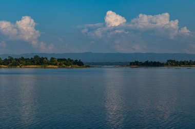 Berrak mavi gökyüzünün altında yuvarlanan yeşil tepelerle çevrili, sakin, mavi sularıyla Kaptai Gölü 'nün huzurlu bir ufkunda manzara ve seyahat fotoğrafçılığı için mükemmel, dingin doğal güzellikleri yakalıyor..