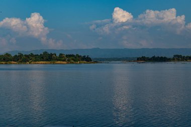 Rangamati Tepesi manzarası, Kaptai Gölü 'nün mavi sularıyla pürüzsüz bir şekilde birleşiyor, canlı yeşillik ve huzur yansımaları sergiliyor. Doğa, seyahat ve manzara fotoğrafçılığı için mükemmel..