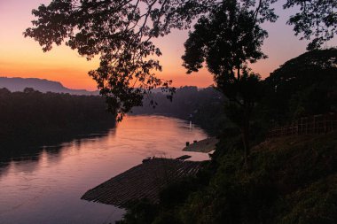 Bandarban, Bangladeş 'teki Sangu Nehri üzerinde, sakin sularda yüzen ağaçlar ve bambu sallarla altın portakallı günbatımı. Huzurlu bir nehir manzarası doğal güzellikleri, huzurlu yansımaları ve huzurlu akşam cazibesini sergiliyor..