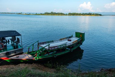 Geleneksel tekneler Bangladeş 'in Kaptai Gölü kıyısında yüzer, sakin sular ve orman tepeleri sergilenir. Doğa, seyahat, eko-turizm ve tropik dinginliği vurgulayan peyzaj fotoğrafçılığı için idealdir..