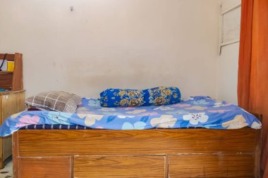 Renkli çiçekli yatak örtüsü ve yastıkla, rahat, tarz ve minimalist iç mekanı vurgulayan, bembeyaz bir arka planı olan, tek bir ahşap yatak. Ev dekorasyonu ve yatak odası fotoğrafçılığı için ideal..