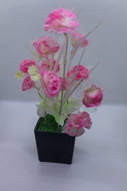 Beyaz bir arka planda izole edilmiş siyah bir tencerede duran yapay pembe karanfil çiçekleri. Ev dekorasyonu, iç tasarım ve çiçek desenleri için ideal. Bakımsız güzellik sunuyor..