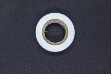 Koyu desenli bir yüzeye yerleştirilmiş temiz, beyaz bir bant rulosunun yakın çekimi. Kontrastı vurgulayan minimalist kompozisyon, ofis arzı, ambalaj malzemesi ve keskin odak ve yüksek çözünürlüklü sabit konsept.