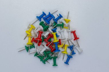 Renkli itme iğnelerinin toplanması yeşil, kırmızı, mavi, sarı ve beyaz, nötr bir yüzeye saçılmış. Notları iğnelemek, tahtaları düzenlemek ve ofis veya okul kullanımı için gerekli kırtasiye malzemeleri.