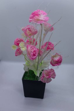 Dekoratif pembe yapay çiçekler zarif bir şekilde siyah bir saksıya yerleştirilmiş. Ev ya da ofis dekorasyonu, masa üstü gösterileri ve fotoğraf malzemeleri için ideal. Canlı, bakımsız güzellik ve şık iç mekan cazibesi sunuyor..