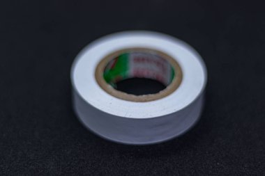 Siyah bir yüzeye izole edilmiş yeni beyaz bant bobini. Elektrik yalıtımı, DIY projeleri ve tamirat için ideal. Kablolama ve bakım işleri için ev, sanayi ve profesyonel kullanım için mükemmel.