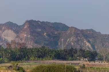 Engebeli bir taşın verimli tropikal yeşillikle güzel zıtlaştığı, çarpıcı ve ahenkli bir manzara yaratan, canlı bir palmiye çiftliğinin üzerindeki doğal kayalık dağ tepesi kuleleri..