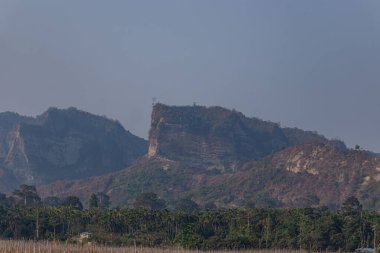 Engebeli dağ uçurumları, yeşil tarlaların kayalık tepelerle buluştuğu kıyı tarım alanlarının ötesinde çarpıcı bir şekilde yükseliyor. Bu da, doğa gücü ve kırsal huzurun çarpıcı bir karışımını oluşturuyor..
