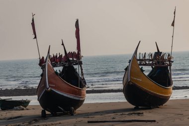 Twin colorful boats stand tall on the sandy shore, facing the gentle waves of the Bay of Bengal. A serene coastal view capturing tradition, tranquility, and the timeless charm of seaside life.