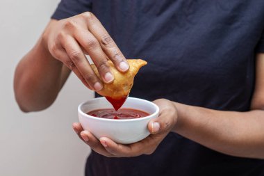 a lady dipping Samosa on tomato sauce. Indian street food.  clipart
