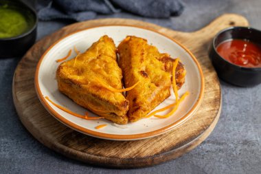 Siyah seramik tabakta yeşil pudina sosu ve domates sosuyla servis edilen Hint atıştırmalığı 