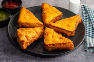 Siyah seramik tabakta yeşil pudina sosu ve domates sosuyla servis edilen Hint atıştırmalığı 