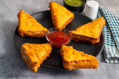 Siyah seramik tabakta yeşil pudina sosu ve domates sosuyla servis edilen Hint atıştırmalığı 