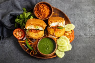 selective focus of Mumbai's famous street food delicious Vada Pav, With coriander leave chutney, tomato sauce, dry garlic chutney and fried chilli.  clipart