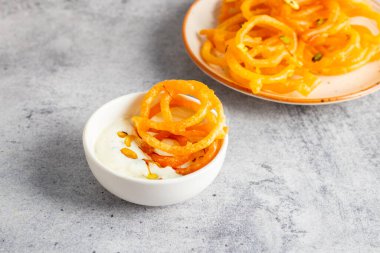 Altın sarısı, sarmal şekilli jalebiler sıcak servis edilir, kremalı, kakule kaplı hahamlarla eşleştirilir, lezzetli, aromatik ve hoşgörülü bir tatlı deneyimi yaratır..