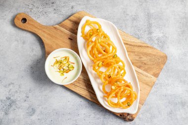 Altın sarısı, sarmal şekilli jalebiler sıcak servis edilir, kremalı, kakule kaplı hahamlarla eşleştirilir, lezzetli, aromatik ve hoşgörülü bir tatlı deneyimi yaratır..