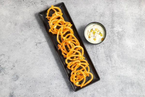 Altın sarısı, sarmal şekilli jalebiler sıcak servis edilir, kremalı, kakule kaplı hahamlarla eşleştirilir, lezzetli, aromatik ve hoşgörülü bir tatlı deneyimi yaratır..