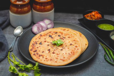 Aloo paratha, baharatlı patates püresiyle doldurulmuş lezzetli bir Hint ekmeği, keskin turşu (achar) ve ferahlatıcı baharatla sıcak servis edilir, mükemmel bir lezzet ve sıcaklık dengesi yaratır..