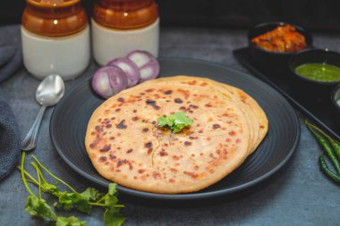 Aloo paratha, baharatlı patates püresiyle doldurulmuş lezzetli bir Hint ekmeği, keskin turşu (achar) ve ferahlatıcı baharatla sıcak servis edilir, mükemmel bir lezzet ve sıcaklık dengesi yaratır..