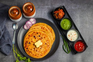 Aloo paratha, baharatlı patates püresiyle doldurulmuş lezzetli bir Hint ekmeği, keskin turşu (achar) ve ferahlatıcı baharatla sıcak servis edilir, mükemmel bir lezzet ve sıcaklık dengesi yaratır..