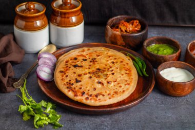Aloo paratha, baharatlı patates püresiyle doldurulmuş lezzetli bir Hint ekmeği, keskin turşu (achar) ve ferahlatıcı baharatla sıcak servis edilir, mükemmel bir lezzet ve sıcaklık dengesi yaratır..