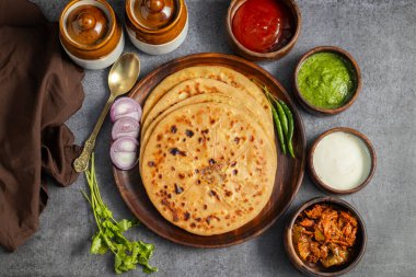 Aloo paratha, baharatlı patates püresiyle doldurulmuş lezzetli bir Hint ekmeği, keskin turşu (achar) ve ferahlatıcı baharatla sıcak servis edilir, mükemmel bir lezzet ve sıcaklık dengesi yaratır..