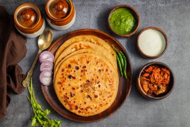 Aloo paratha, baharatlı patates püresiyle doldurulmuş lezzetli bir Hint ekmeği, keskin turşu (achar) ve ferahlatıcı baharatla sıcak servis edilir, mükemmel bir lezzet ve sıcaklık dengesi yaratır..