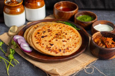 Aloo paratha, baharatlı patates püresiyle doldurulmuş lezzetli bir Hint ekmeği, keskin turşu (achar) ve ferahlatıcı baharatla sıcak servis edilir, mükemmel bir lezzet ve sıcaklık dengesi yaratır..
