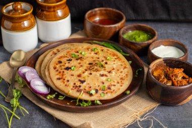 Aloo paratha, baharatlı patates püresiyle doldurulmuş lezzetli bir Hint ekmeği, keskin turşu (achar) ve ferahlatıcı baharatla sıcak servis edilir, mükemmel bir lezzet ve sıcaklık dengesi yaratır..