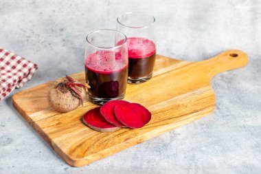 Bir bardak pancar suyu, taze pancar dilimleri, bir pancar kökü ve tahta üzerinde nane yaprakları..