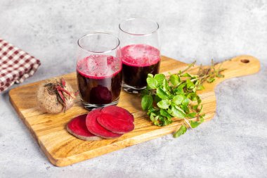 Bir bardak pancar suyu, taze pancar dilimleri, bir pancar kökü ve tahta üzerinde nane yaprakları..